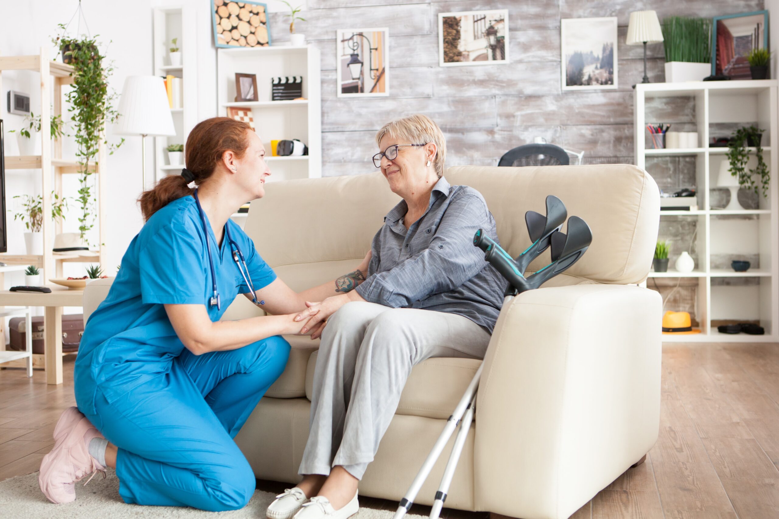 Joyful old lady sitting on couch in a nursing home holding health taker arm.